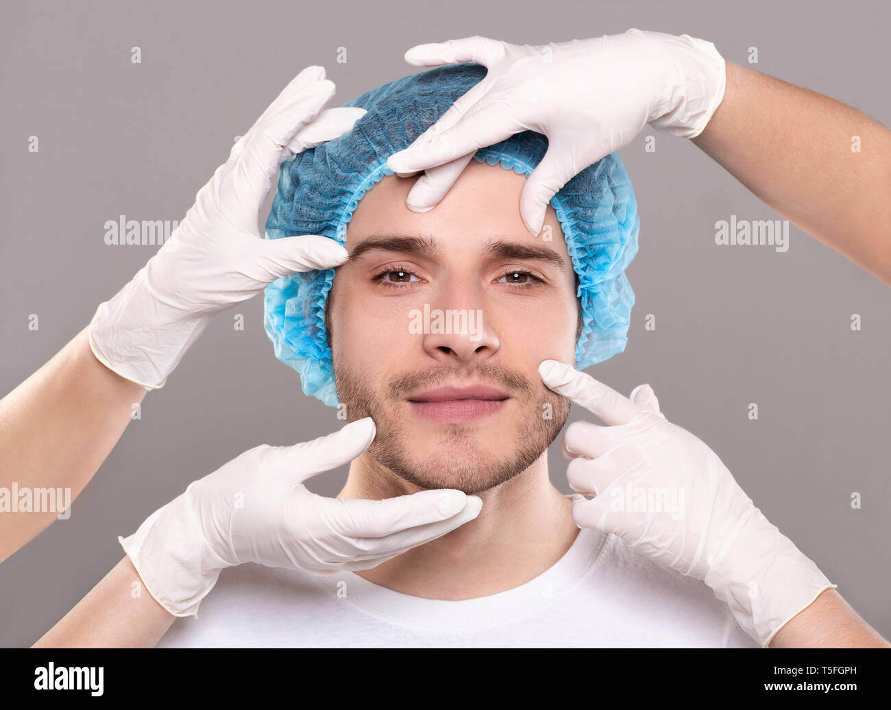 Doctor's Hände in Handschuhen berühren Gesicht von gutaussehenden jungen Mann Stockfoto