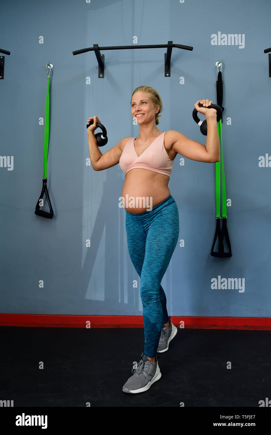 Lächelnd schwangere Frau üben mit den Kettlebells in einem Fitnessstudio Stockfoto