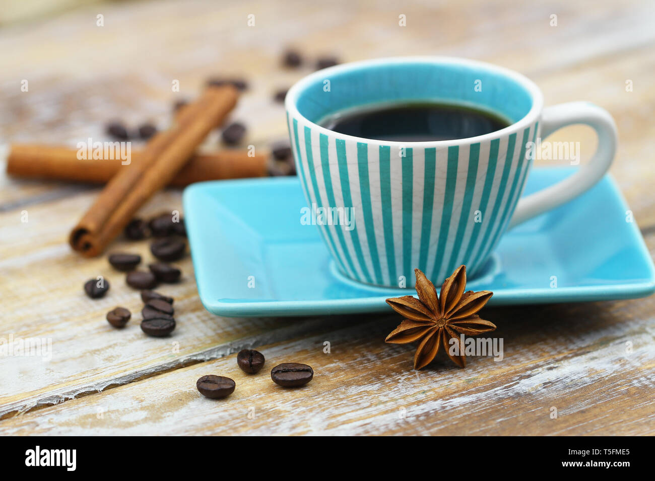 Tasse schwarzen Kaffee in vintage Schale, Sternanis, Zimtstangen und verstreute Kaffeebohnen auf Holz- Oberfläche Stockfoto