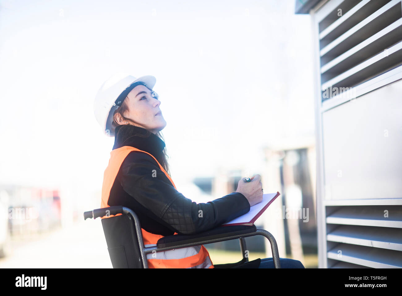 Junge Techniker mit Helm und Weste im Rollstuhl im Freien arbeiten Stockfoto
