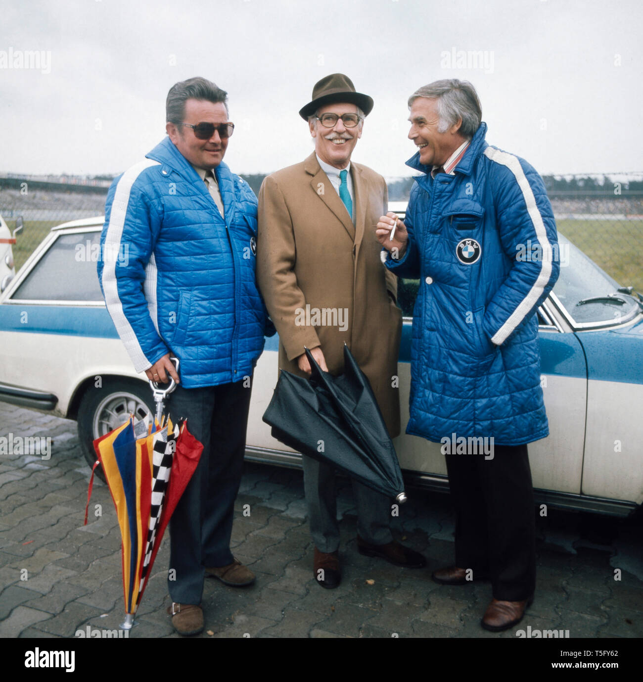 Joachim Fuchsberger unerhält sich mit 2 anderen Leuten vor einem Auto und raucht dabei eine Zigarette, Deutschland 1970er. Joachim Fuchsberger ist Holding mit 2 weiteren Personen in einem Auto und raucht eine Zigarette, Deutschland 1970 s Stockfoto