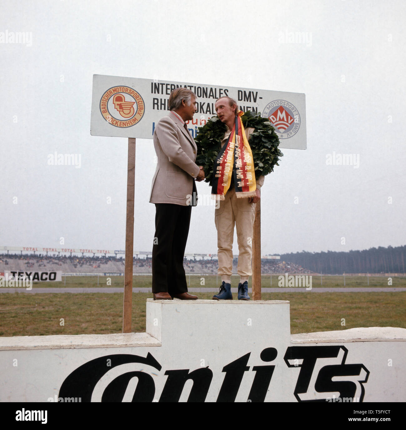 Joachim Fuchsberger e auf einem Podest und gratuliert dem Sieger des Rennens im, Hockenheimring, Deutschland Ca. 1970er. Joachim Fuchsberger steht auf einem Podium und gratuliert dem Gewinner der Rennen auf dem Hockenheimring, Deutschland ca. 1970 s Stockfoto