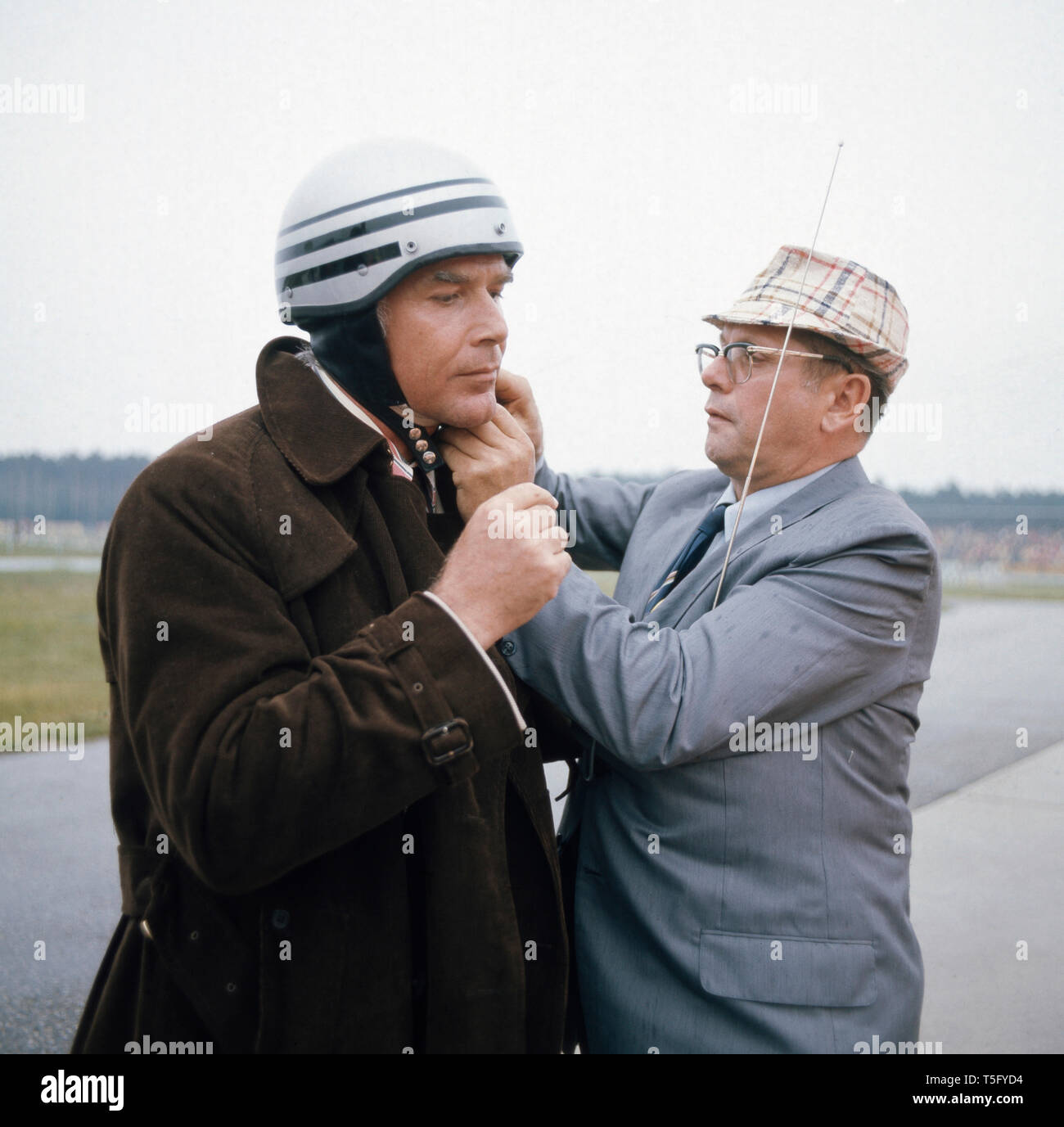 Joachim Fuchsberger wird bei dem Anziehen eines Helmes geholfen, Ca. 1970. Joachim Fuchsberger wird durch einen Helm anziehen geholfen, Ca. 1970 Stockfoto