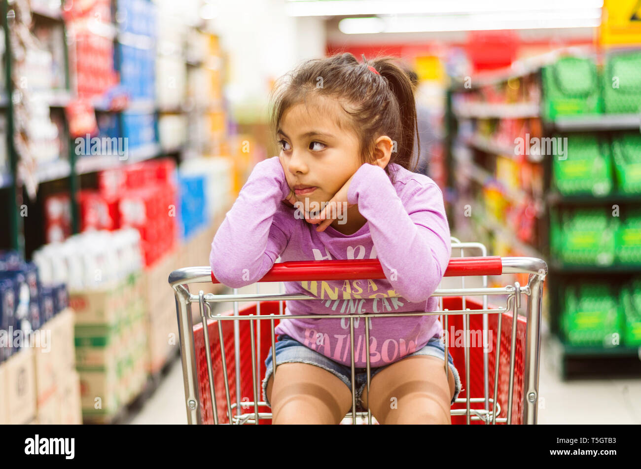 Verkauf, Konsumismus und Personen Konzept - glückliche kleine Mädchen nachdenklich im Warenkorb im Supermarkt Stockfoto