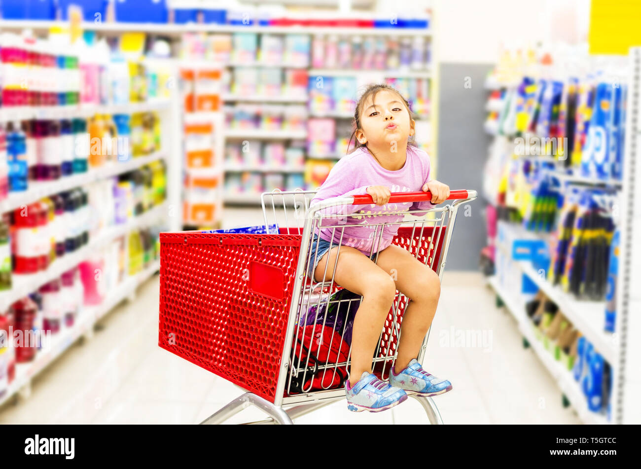 Verkauf, Konsumismus und Personen Konzept-fröhliches kleines Mädchen in Warenkorb im Supermarkt Stockfoto