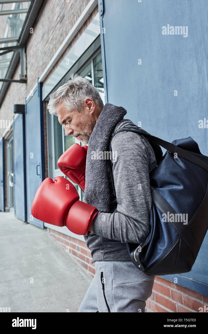 Reifer Mann mit Handtuch, Sporttasche und roten Boxhandschuhe vor der Turnhalle stand Stockfoto