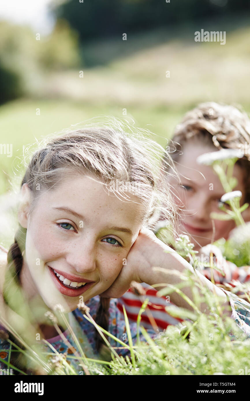 Portrait von lächelnden Mädchen liegt auf einer Wiese mit kleinen Bruder im Hintergrund Stockfoto