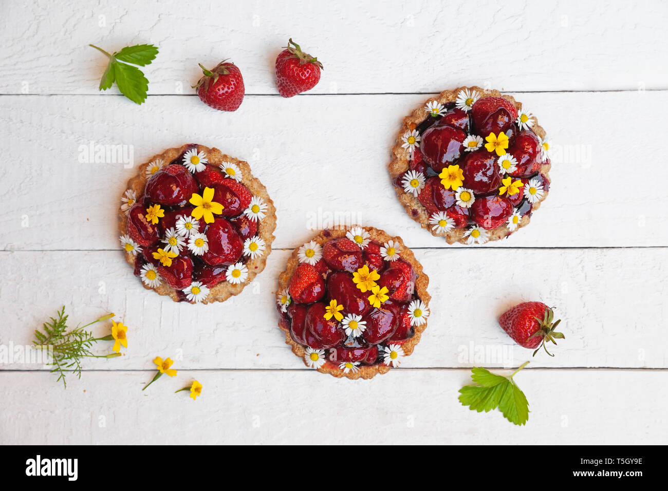 Selbstgemachte Erdbeer Herz Törtchen mit Daisy Blumen und goldenen Ringelblumen, essbare Blüten, weiß Holz Stockfoto