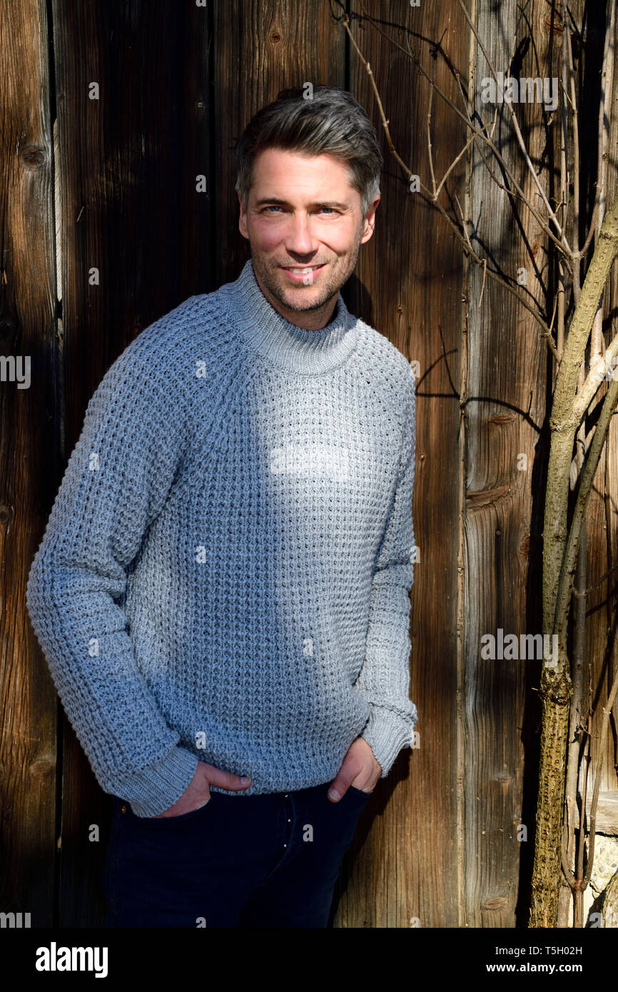 Portrait von reifer Mann mit ergrauendem Haar und grauen pullover, Hände in den Taschen Stockfoto