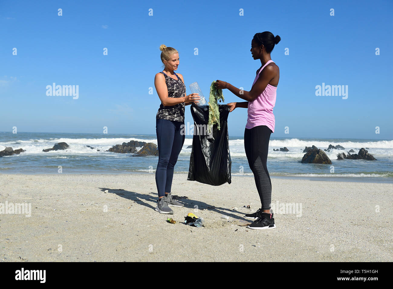 Zwei Frauen, die Reinigung, die den Strand von Kunststoffabfällen Stockfoto