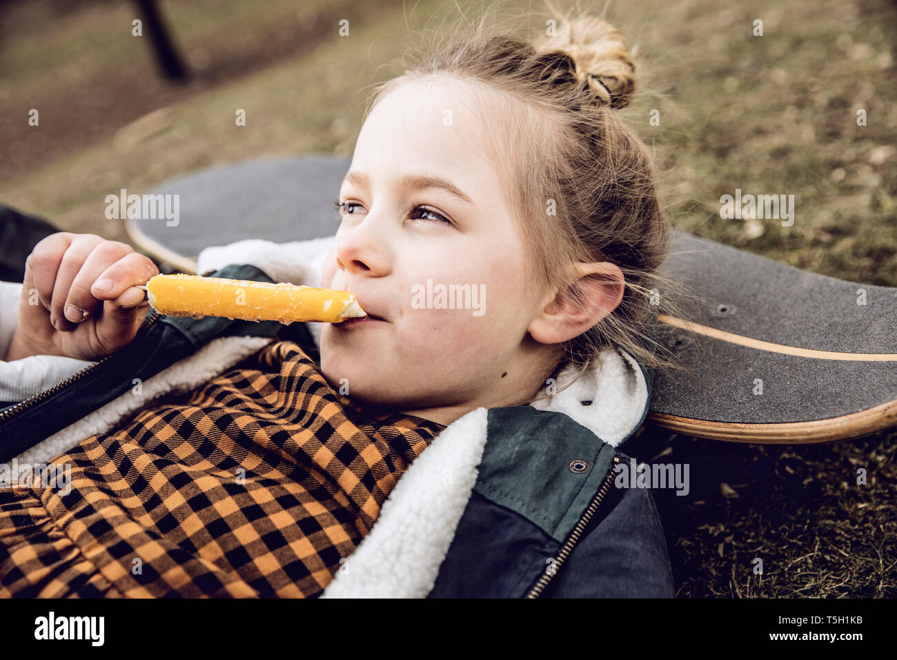 Kleines Mädchen essen Eis, ruhender Kopf auf Skateboard Stockfoto