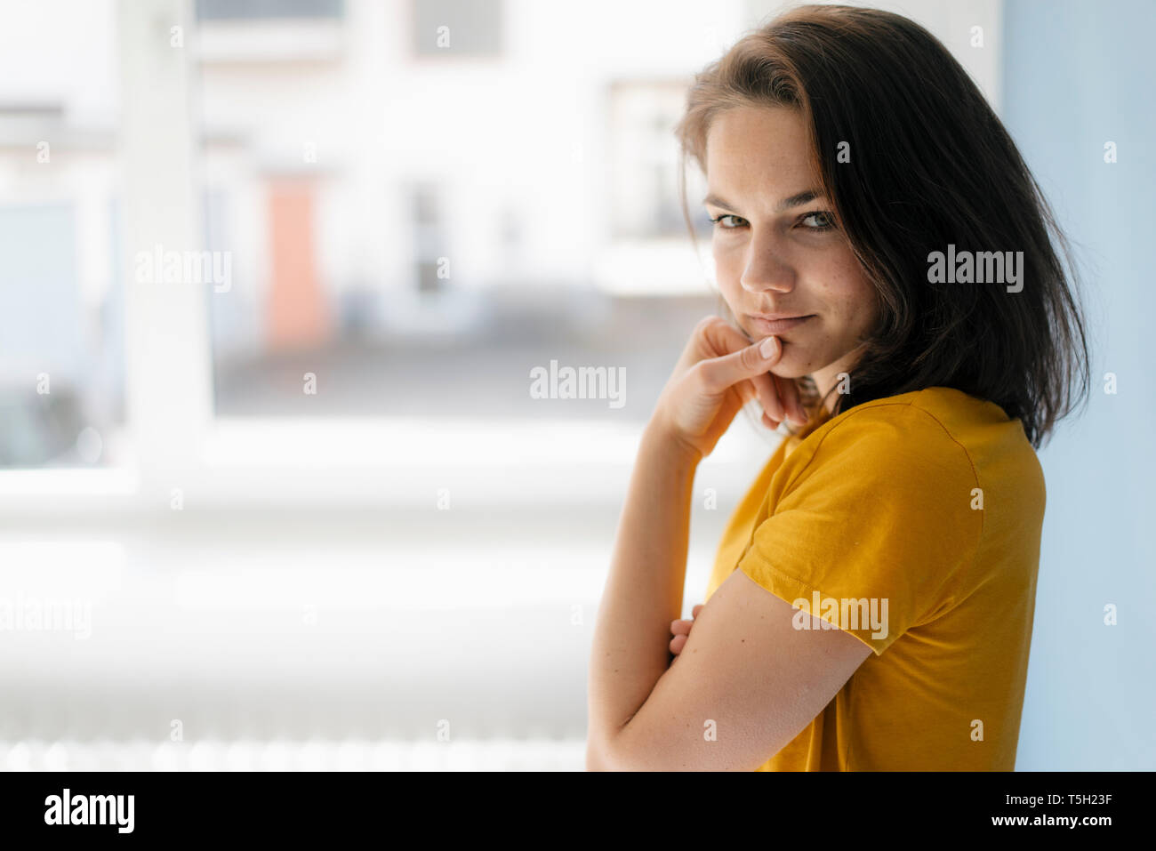 Pretty Woman standing gegen Fenster, mit der Hand am Kinn, denken Stockfoto