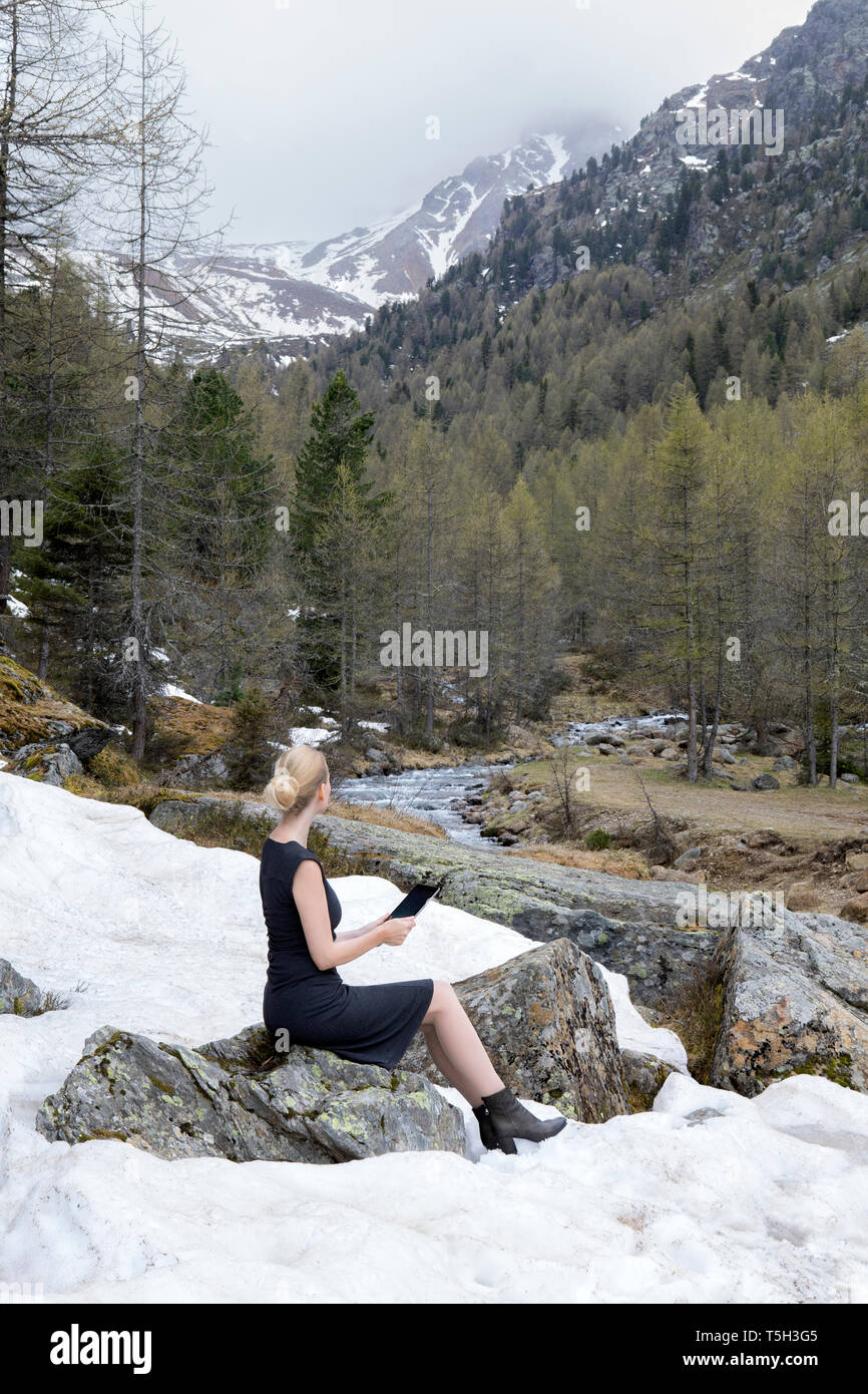 Italien, Südtirol, Ultental, Frau sitzt in schneebedeckten Berg Tal mit Tablet Stockfoto
