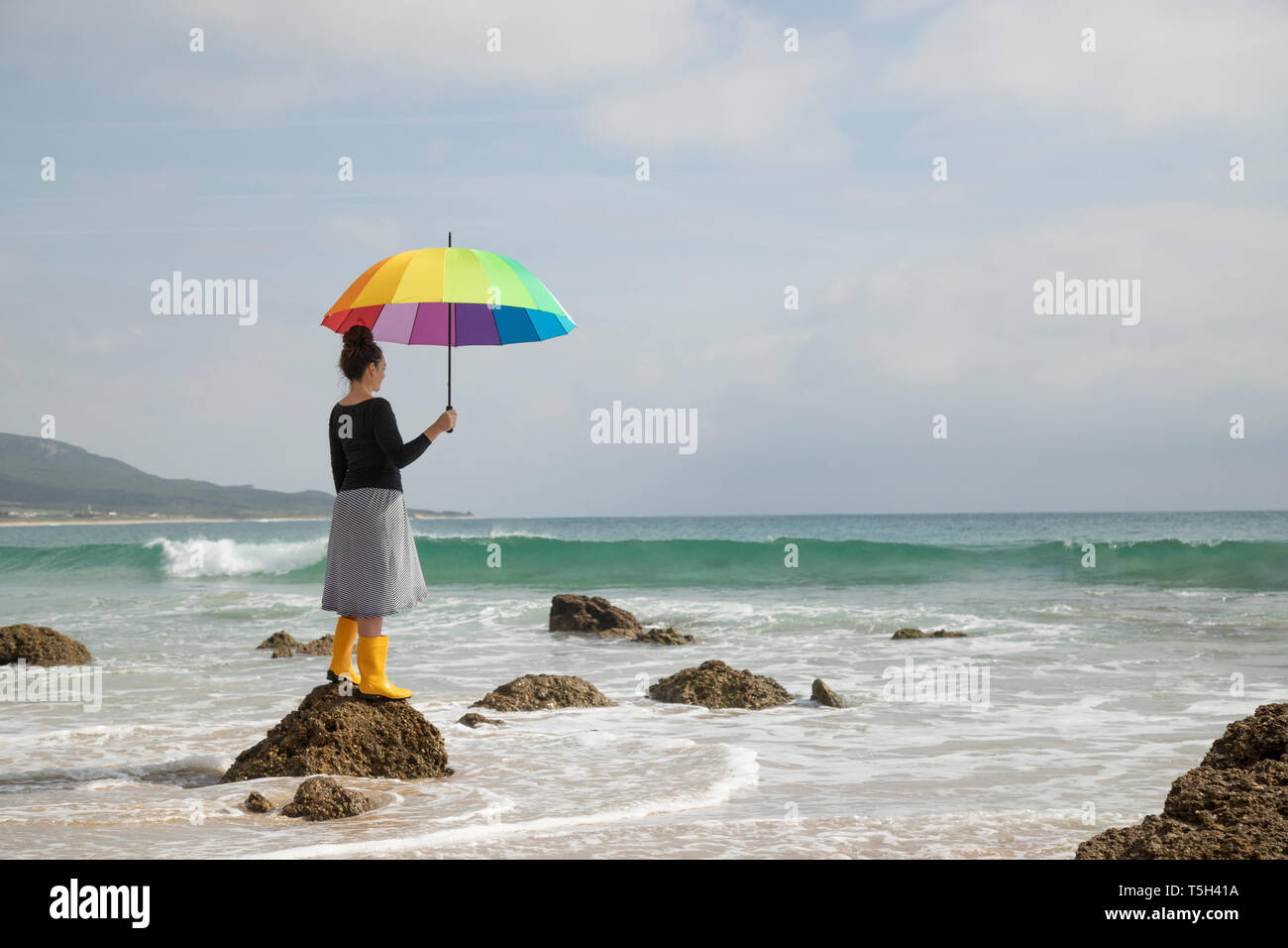Frau mit bunten Regenschirm stehen auf einem Stein am Strand Stockfoto