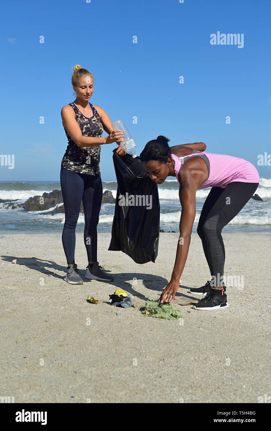 Zwei Frauen, die Reinigung, die den Strand von Kunststoffabfällen Stockfoto