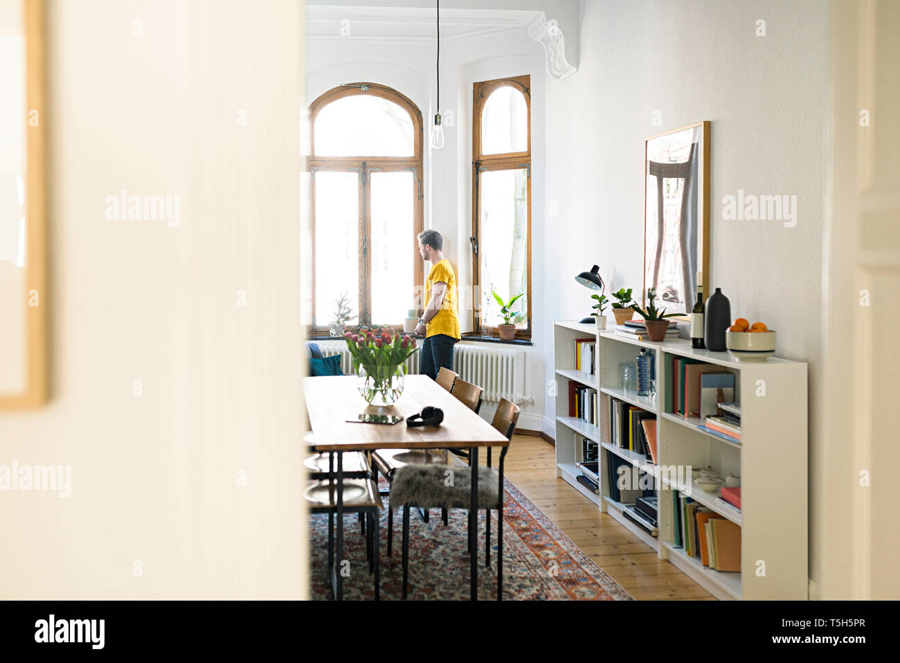 Legerer Mann im gelben Shirt in stilvolles Apartment Blick aus Fenster Stockfoto