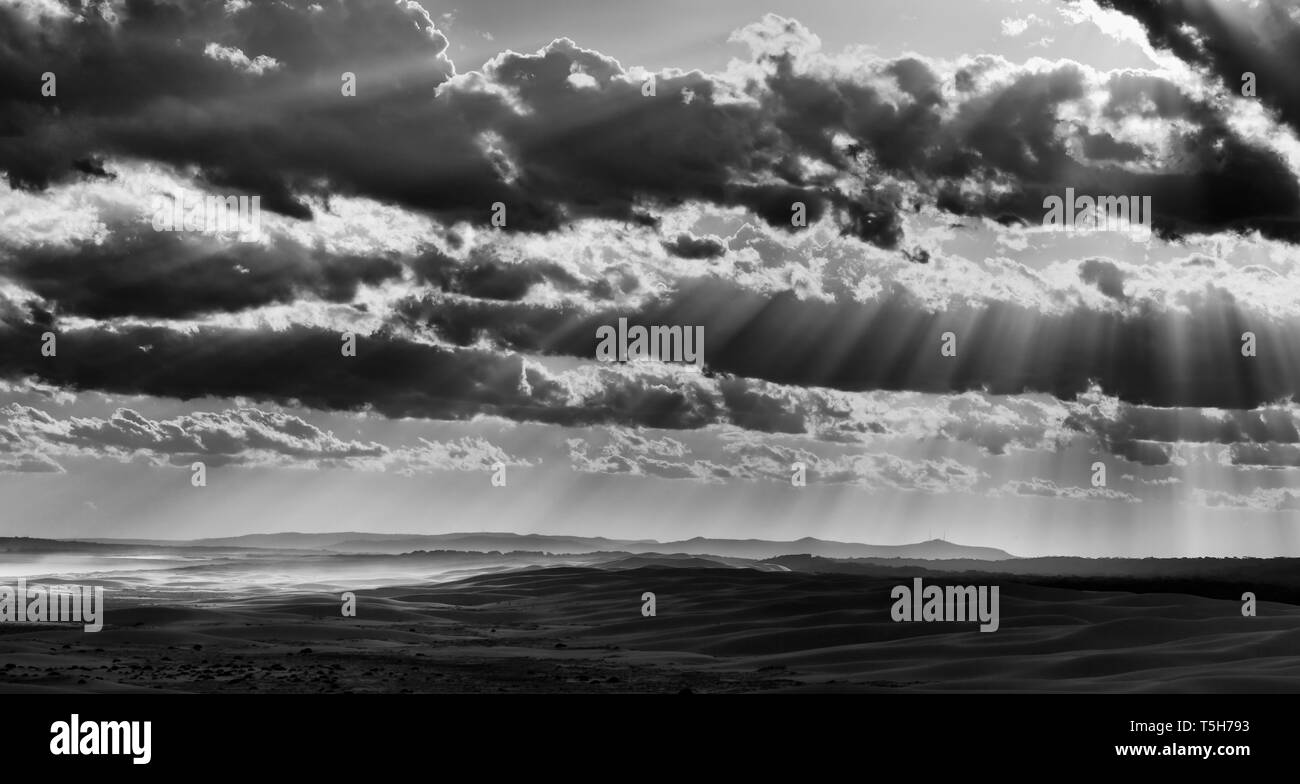 Kontrast runrays Schneiden durch mehrschichtige Wolken über Sanddünen an der Pazifikküste von Ausralia um Stockton Strand bei Sonnenuntergang zu Schwarz Weiß umgewandelt Stockfoto