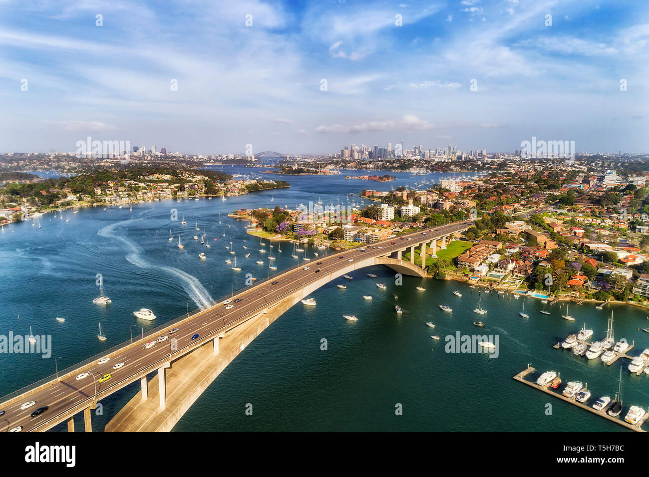 Konkrete Bogen von Gladesville Brücke über Parramatta River in Sydneys Innerem Westen mit Blick auf die weit entfernte Stadt Sydney CBD und lokalen Marina angedockt Floating y Stockfoto