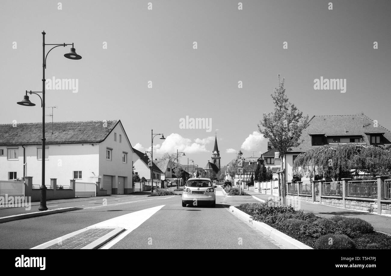 Bergheim, Frankreich - 19 April 2019: Ruhiges Dorf von Bergheim schwarz/weiß-Bild mit Hauptstraße mit VW Golf Auto, Häuser und Kirche Turm Stockfoto