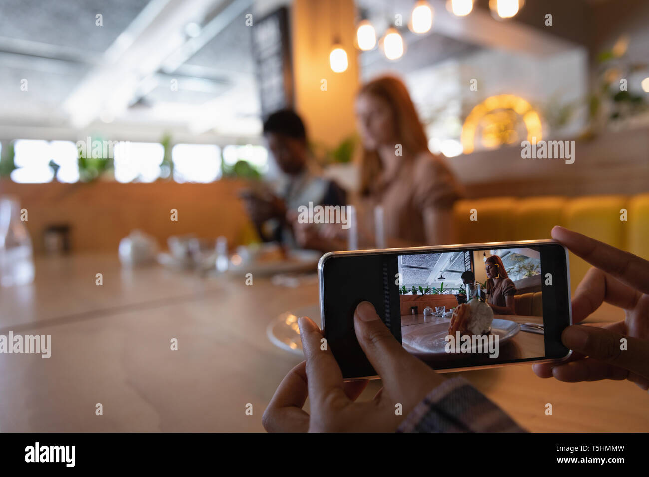 Weibliche Freunde unter Foto von Frühstück essen mit Handy Stockfoto