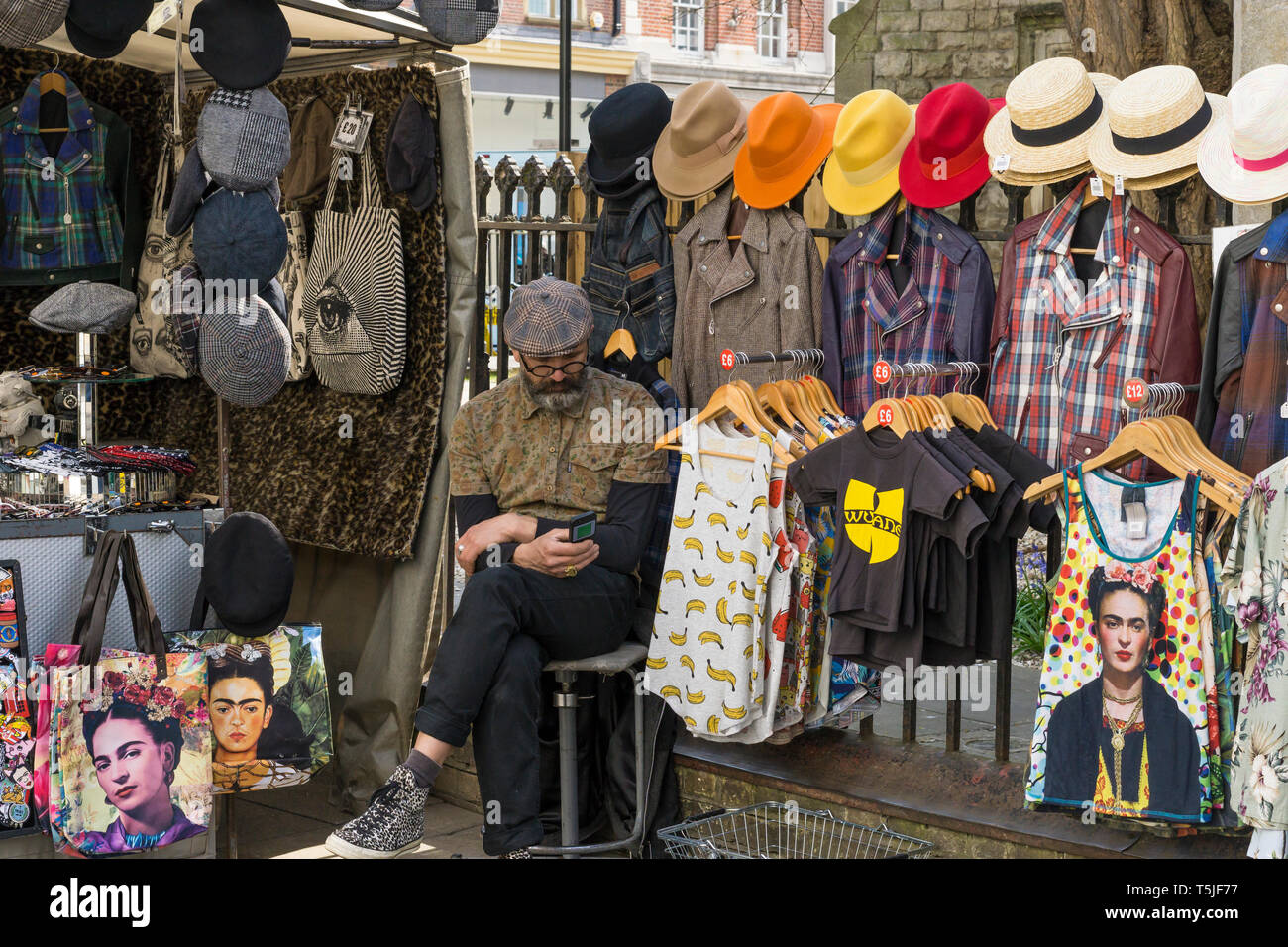 Standbesitzer auf Handy, Kleidung und Hut auf der Market Street Cambridge Abschaltdruck Stockfoto