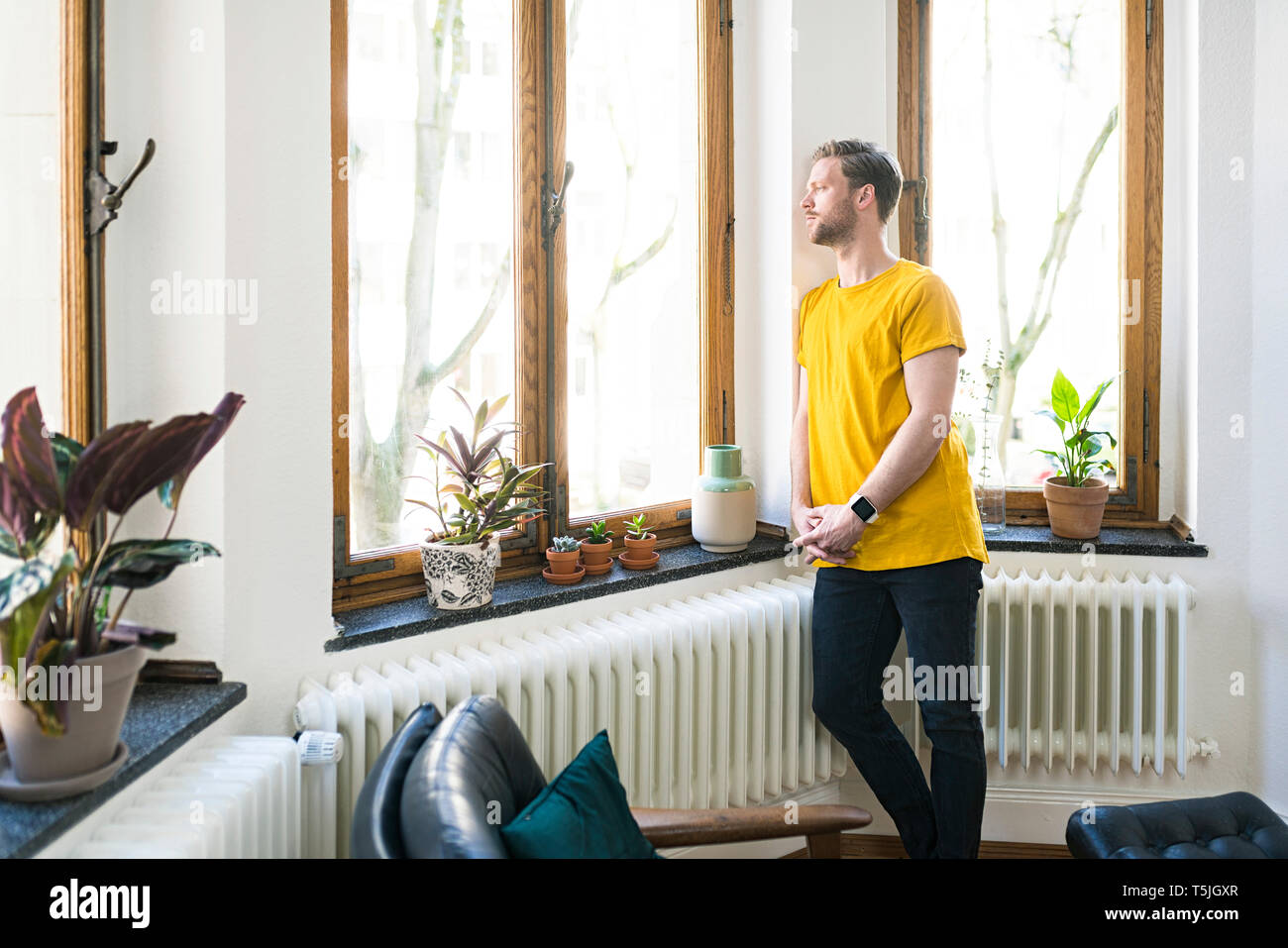 Nachdenklicher Mann im gelben Shirt in stilvolles Apartment Blick aus Fenster Stockfoto