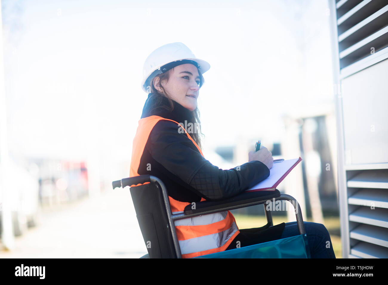 Junge Techniker mit Helm und Weste im Rollstuhl im Freien arbeiten Stockfoto