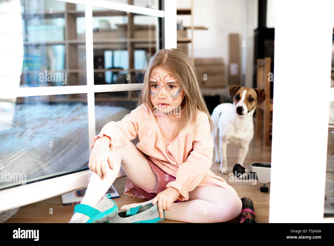 Blonde Mädchen, die als Schmetterling auf dem Boden sitzend, Jack Russel Terrier im Hintergrund Stockfoto
