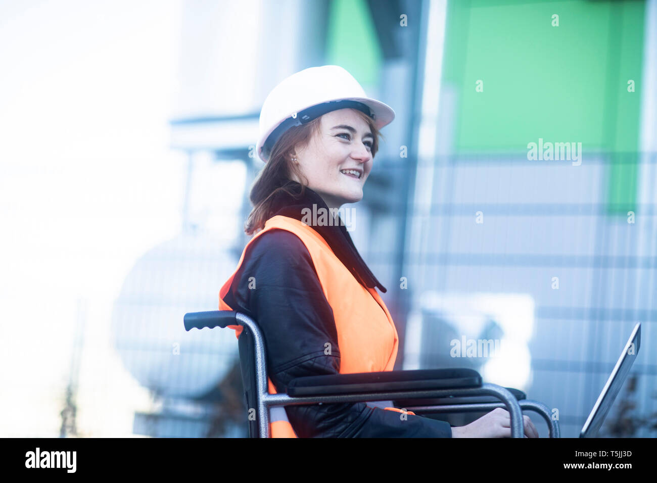 Junge Techniker mit Helm und Weste im Rollstuhl Arbeiten am Laptop im Freien Stockfoto