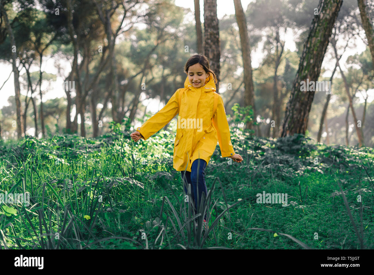 Lächelnde Mädchen tragen gelbe Regenmantel und Wandern im Wald Stockfoto