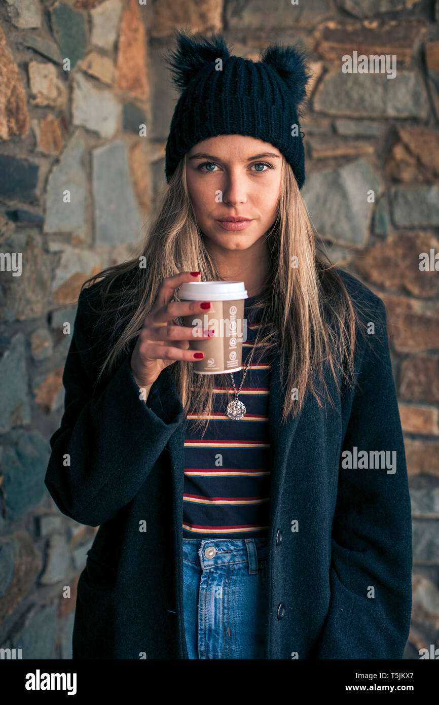 Porträt der jungen Frau mit Kaffee trinken gehen das Tragen von Mantel und Mütze Stockfoto