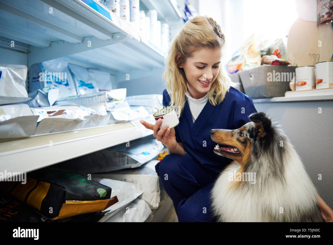 Junge Frau, die Essen für einen Hund von Regal des Tierarztes Stockfoto