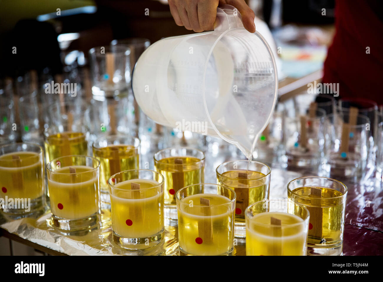 In der Nähe der Person gießt flüssiges Wachs für handgemachte Kerzen in Gläsern. Stockfoto