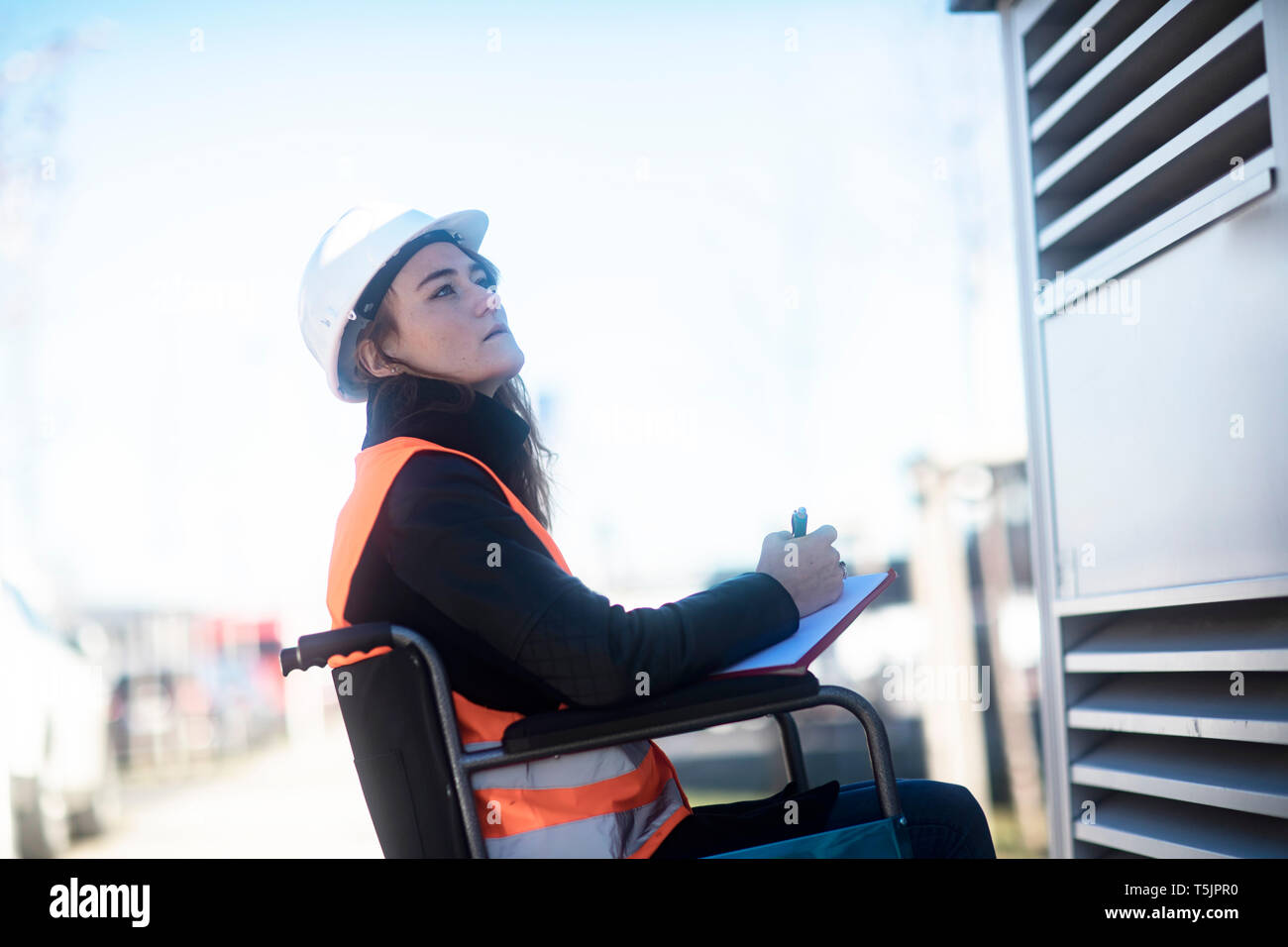 Junge Techniker mit Helm und Weste im Rollstuhl im Freien arbeiten Stockfoto