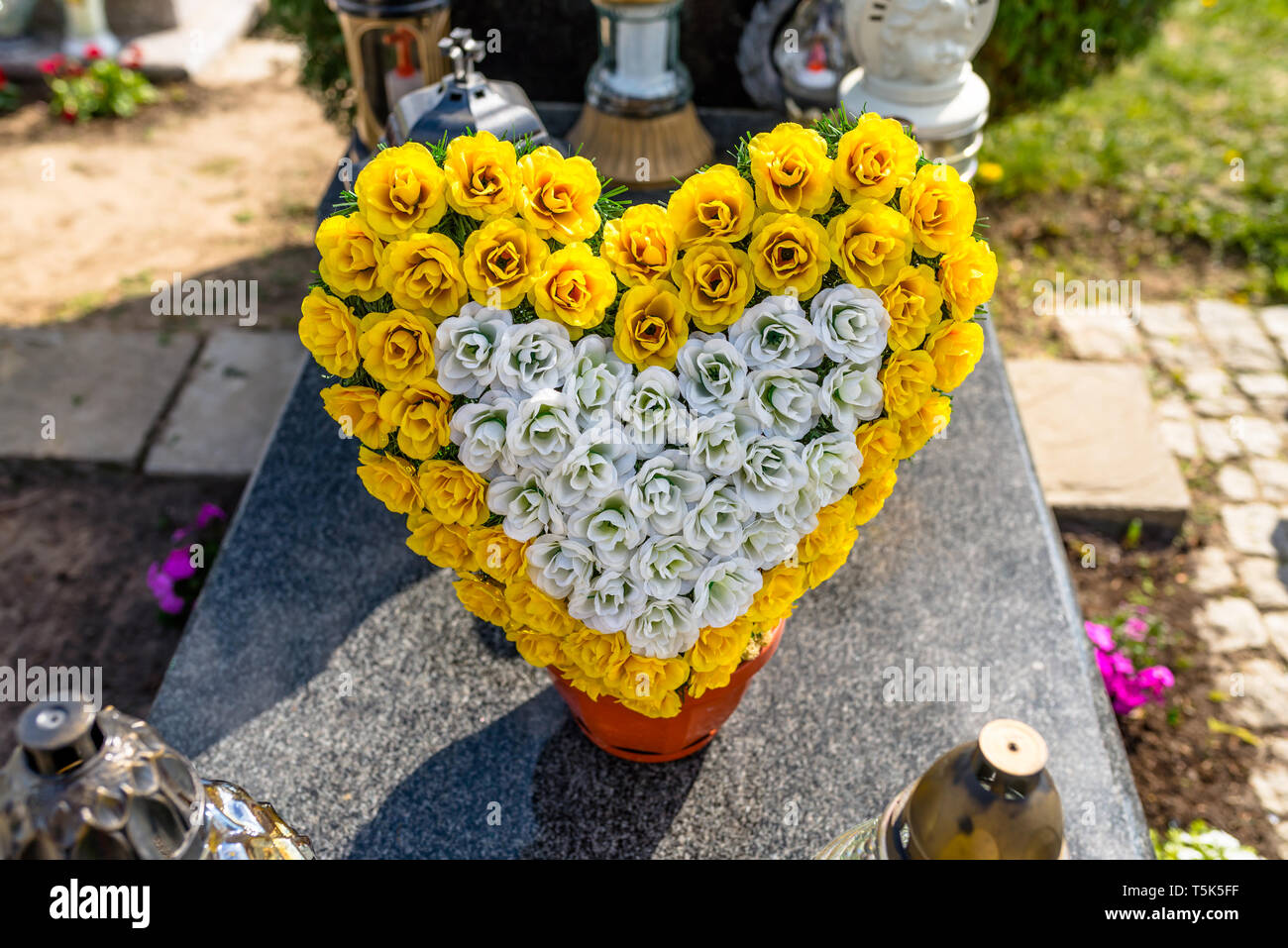 Künstliche Blumen in der Form eines Herzens und Kerzenständer liegen auf dem Grabstein auf dem Friedhof Stockfotografie