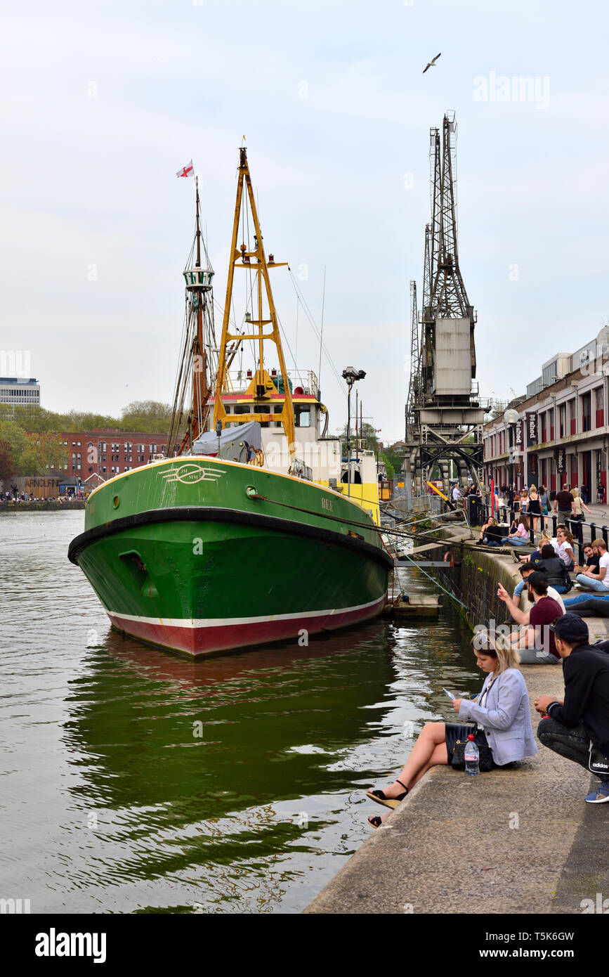 Bristol Schwimmenden Hafen, Leute sitzen auf Wapping Wharf Kai mit versorgungsschiff Biene von Bristol und historischen elektrischen Krane Stockfoto