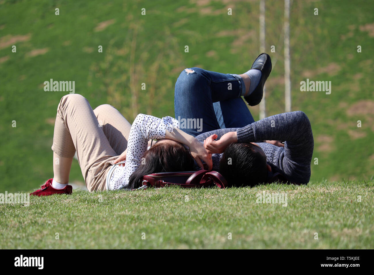 Glückliches Paar liegt auf einem grünen Hügel an einem warmen sonnigen Tag, Frühling Saison. Kerl und ein Mädchen in einem Park, romantische Liebe Datum auf frisches Gras Stockfoto