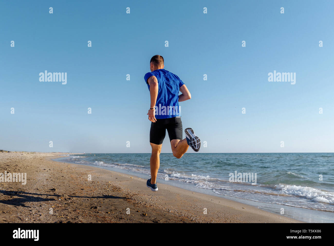Zurück man Athleten, die auf sandigen Strand Hintergrund blauer Himmel Stockfoto