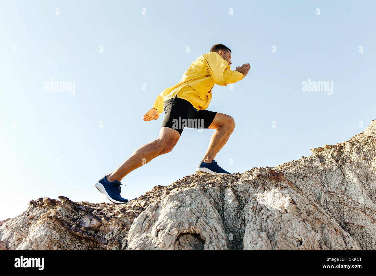 Man klettert bergauf Berg in gelber Jacke Hintergrund Himmel Stockfoto