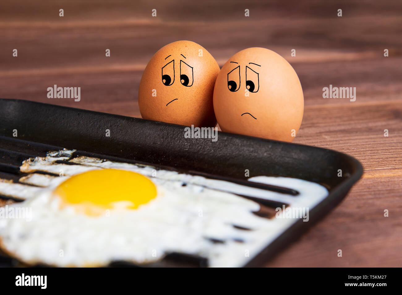 Eier mit einem traurigen Gesicht in der Nähe ein Spiegelei. Humorvoll Bild. Urlaub Ostern. Gesunde Lebensmittel für Frühstück. Stockfoto