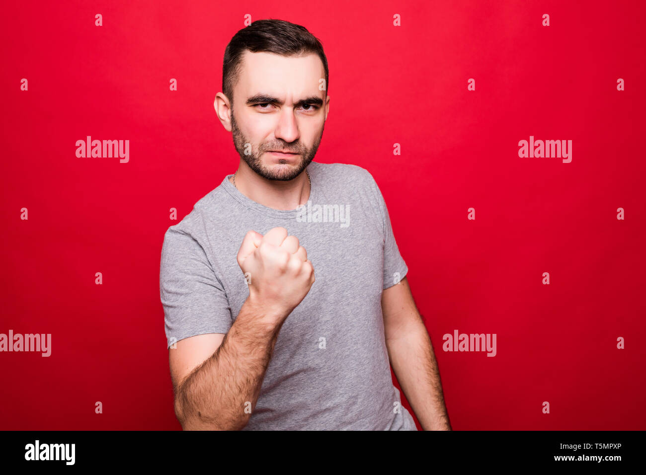 Angry Young Man Show geballte Faust drohen oder Warnung geben auf Roten studio Hintergrund isoliert Gefahr oder Bedrohung zeigen Stockfoto