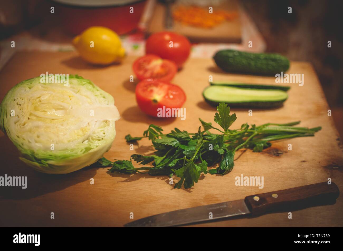 Gemüsescheiben in dem Holzbrett. Kohl, Tomaten, Gurken, Zitrone und Petersilie Stockfoto