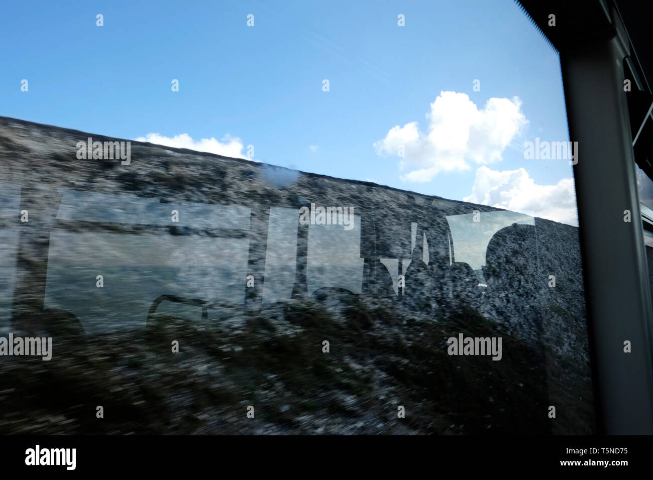 Silhouette Reflexion in einem Bus-Fenster von einem Bus Interieur und der Blick aus dem Fenster auf das Meer Horizont mit blauem Himmel und weißen Wolken darüber hinaus. Stockfoto