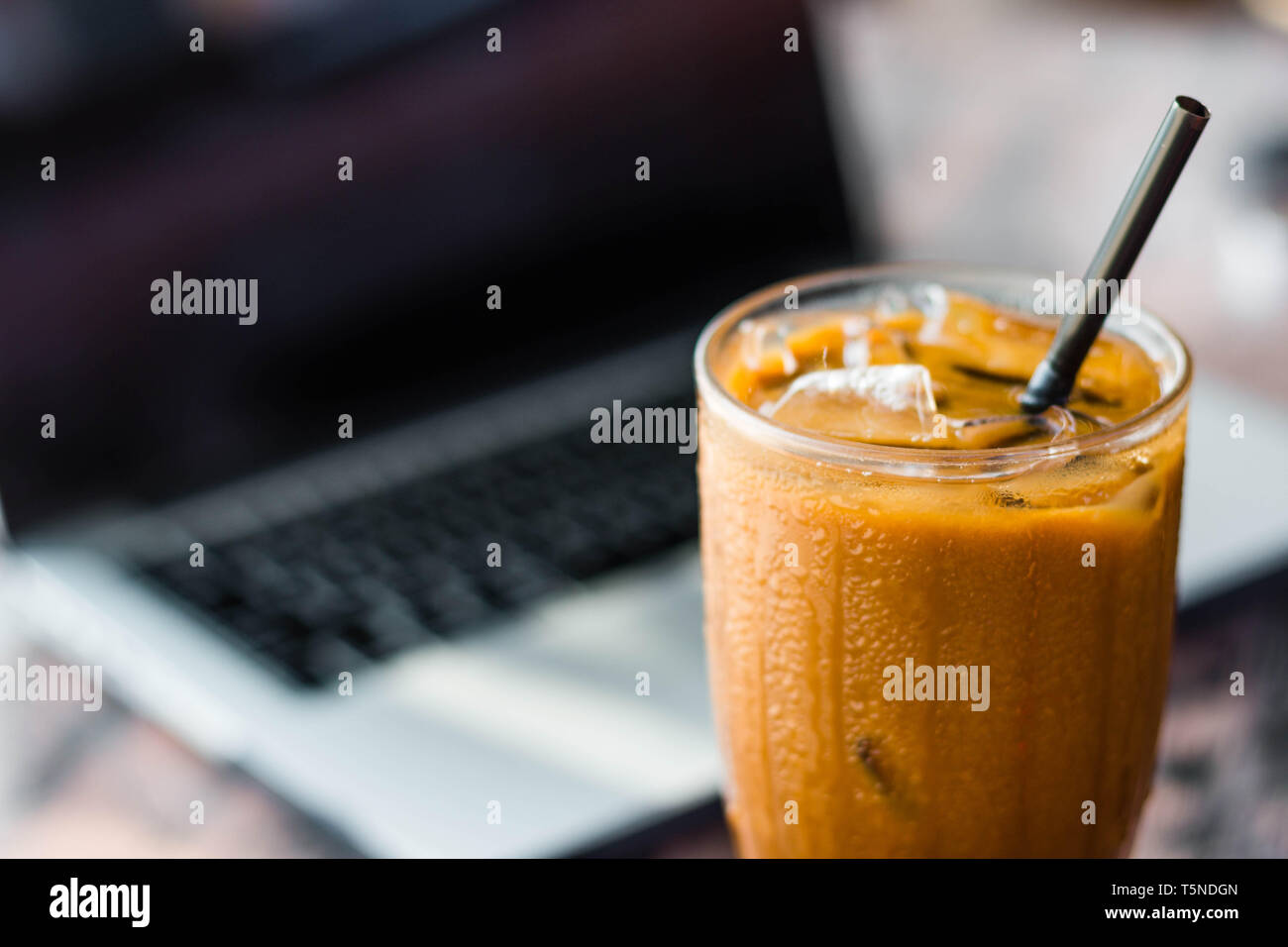 Eis Kaffee in eine Tasse mit einem Laptop auf dem Hintergrund. Freelancer Konzept und Arbeit an Feiertagen Idee. Stockfoto