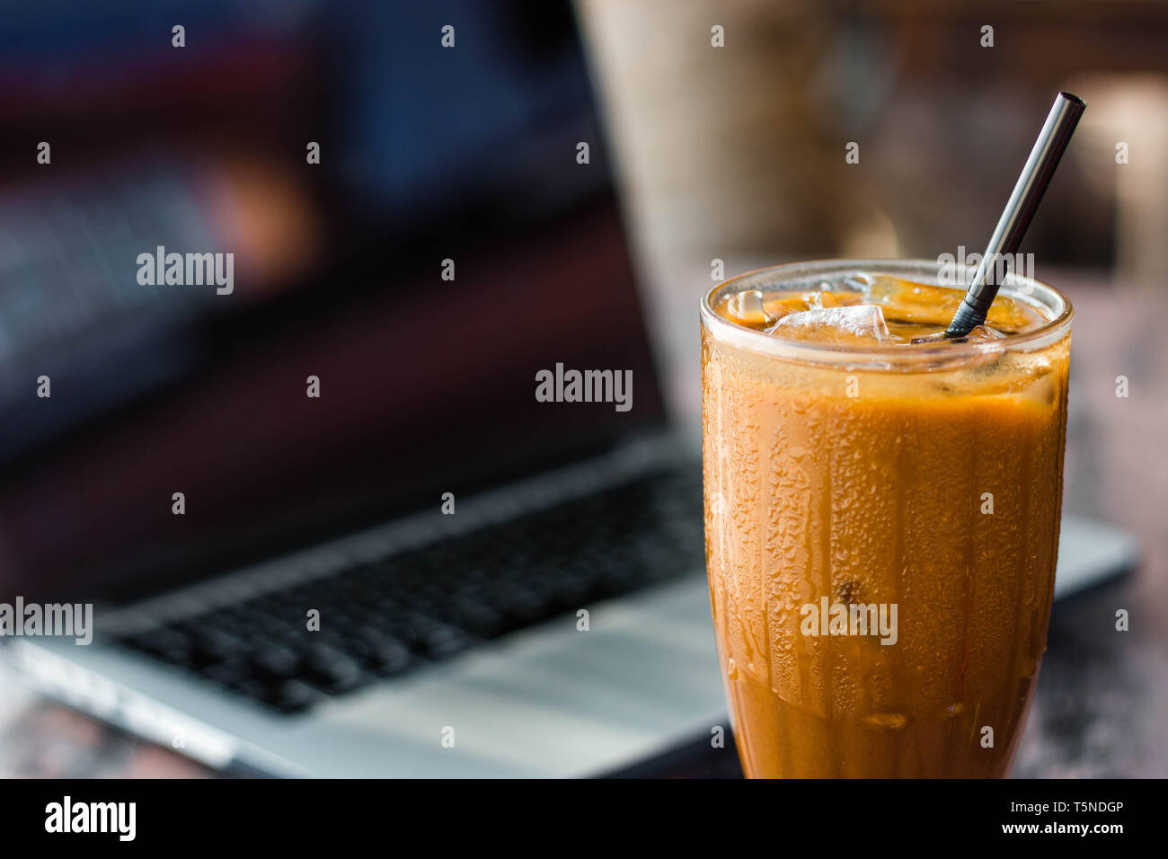 Eis Kaffee in eine Tasse mit einem Laptop auf dem Hintergrund. Freelancer Konzept und Arbeit an Feiertagen Idee. Stockfoto