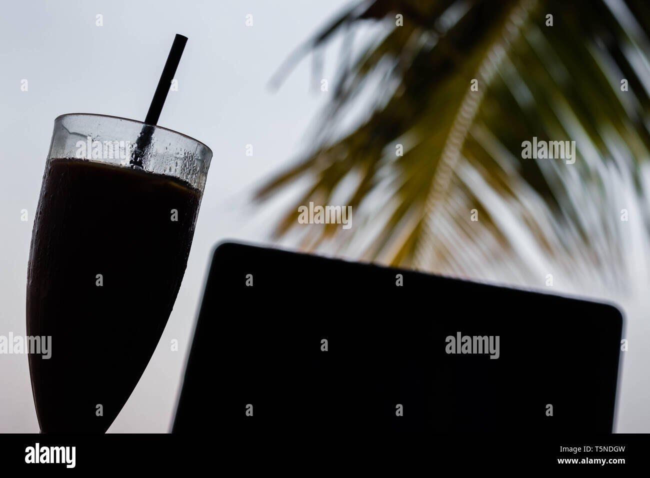 Hintergrundbeleuchtung der Eiskaffee und einen Computer auf dem Tisch vor dem Strand Stockfoto