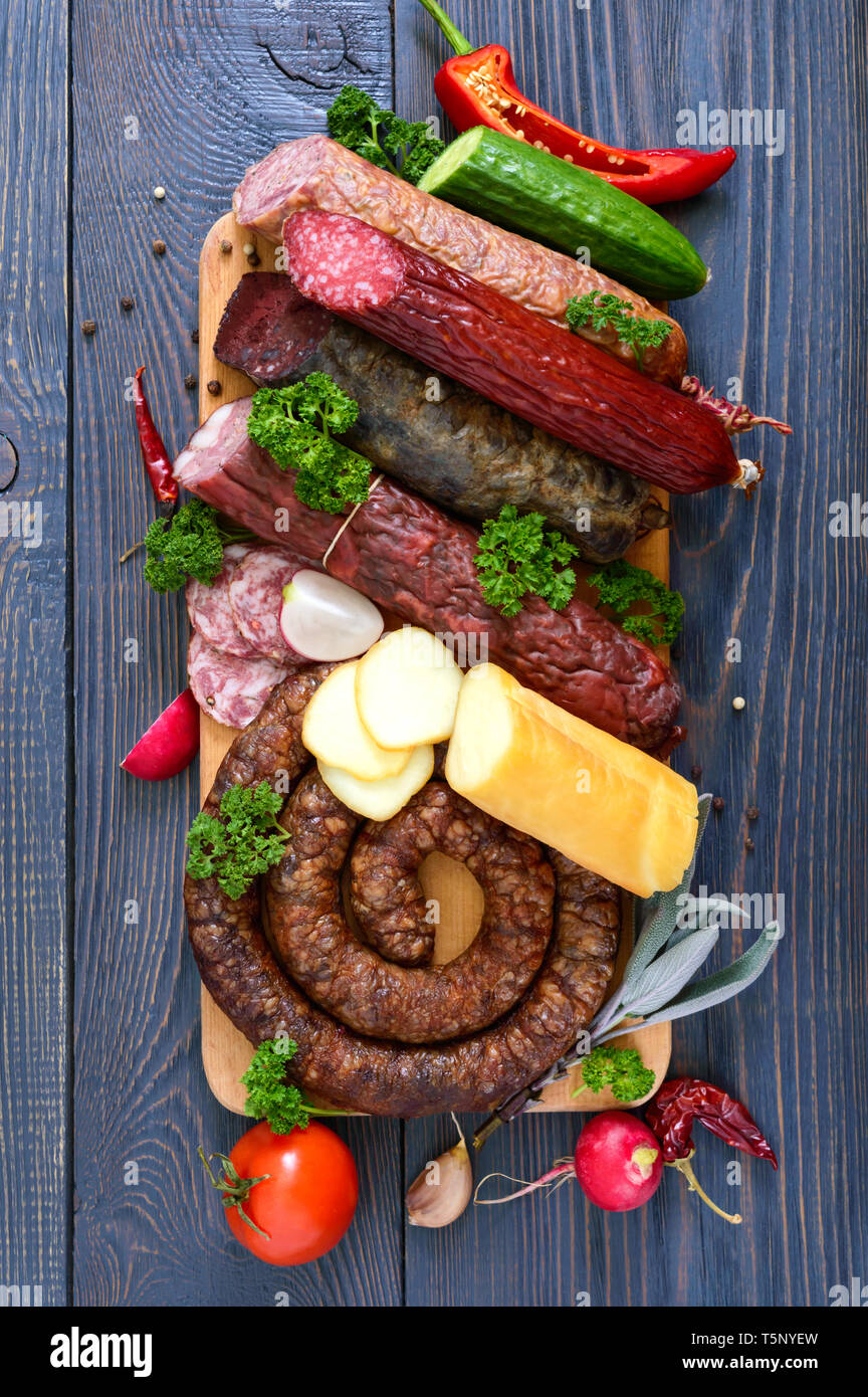 Viele Arten von Wurst, geräucherter Käse, frisches Gemüse auf einem hölzernen Hintergrund. Produkte in den Urlaub. Ansicht von oben. Flach. Stockfoto