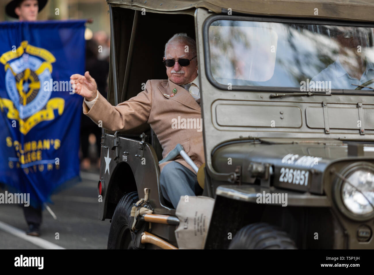 Eine ältere zurück Veteran in seinem Begleitfahrzeug winken und geben Daumen bis zu der Menge jubeln und klatschen für ihn, während der ANZAC Day März Stockfoto