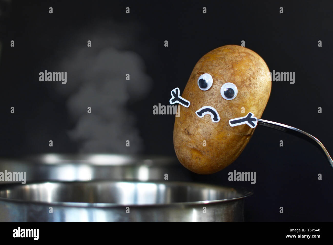 Kartoffel mit traurigem Gesicht und goggle Augen in einem dampfenden Kochtopf auf dunklen schwarzen Hintergrund gesetzt werden Stockfoto