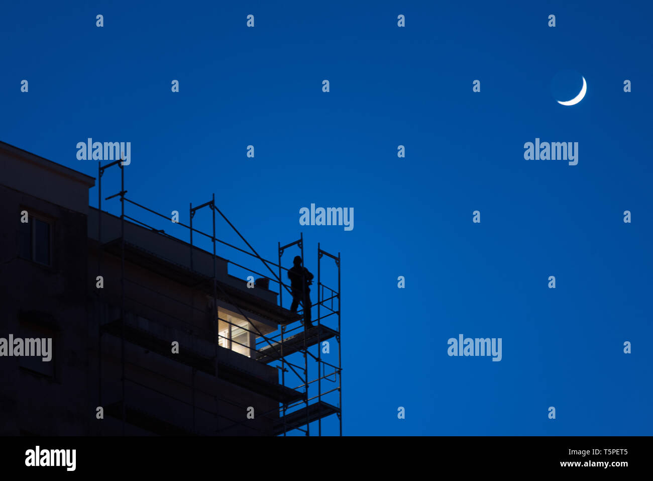 Silhouette der Mann bei der Arbeit hoch oben auf einem Wolkenkratzer Gerüst bei Dämmerung, gefährliche Arbeit, Sicherheit am Arbeitsplatz, blauer Himmel mit Mond im Hintergrund Stockfoto